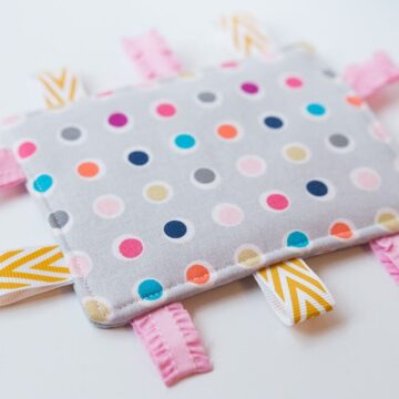 Taggie Baby Toy - a simple sewing project perfect for any new baby. Colorful ribbons and a bright pattern makes this a great sensory toy for your little one.