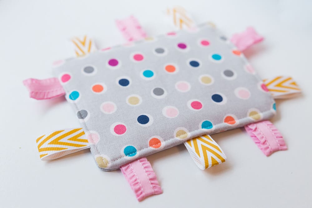 Taggie Baby Toy - a simple sewing project perfect for any new baby. Colorful ribbons and a bright pattern makes this a great sensory toy for your little one. 