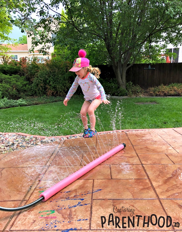 Little Girl playing in pool noodle sprinkler
